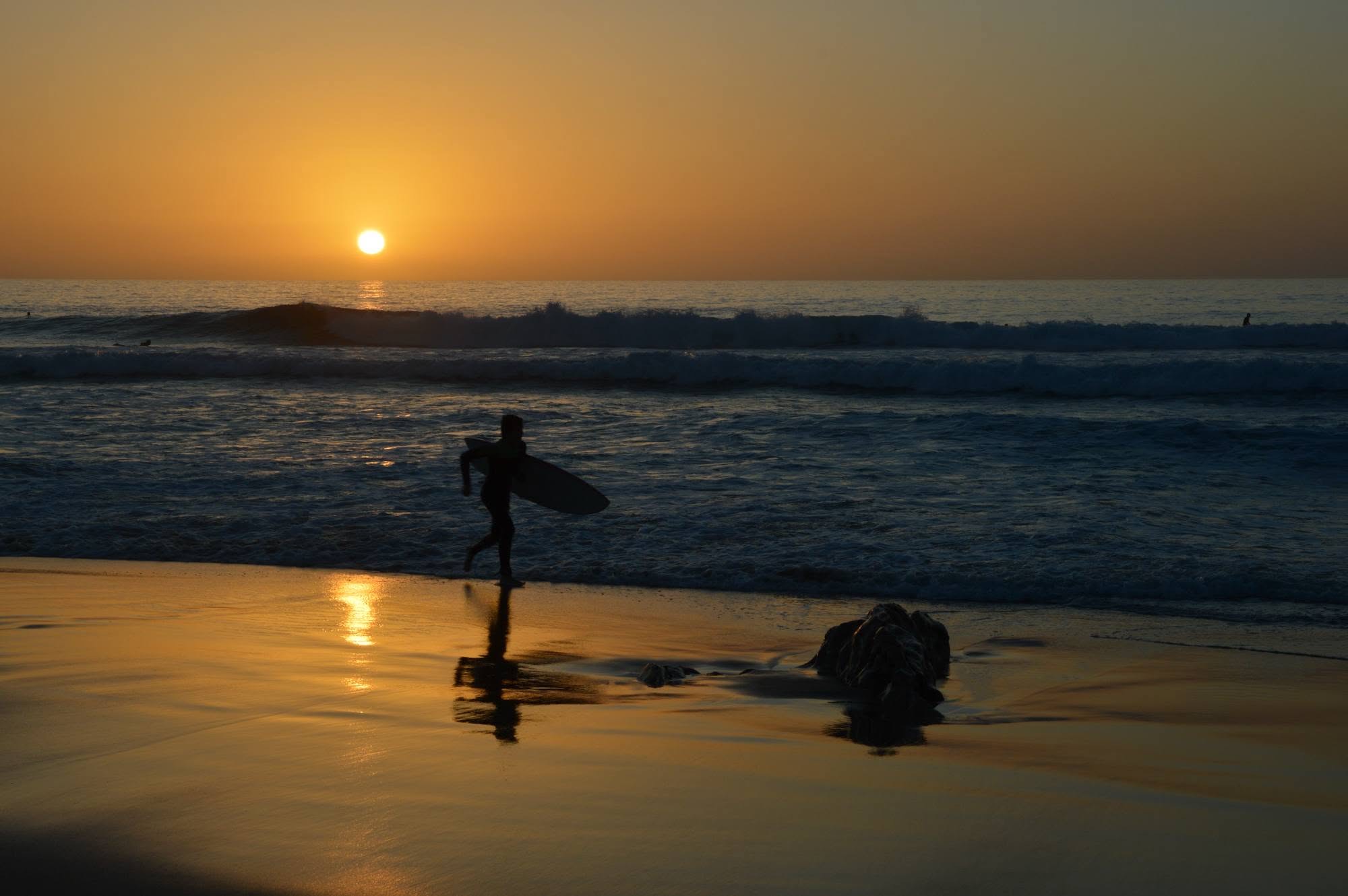 Un surfista cammina verso l'oceano al tramonto, a Fuerteventura
